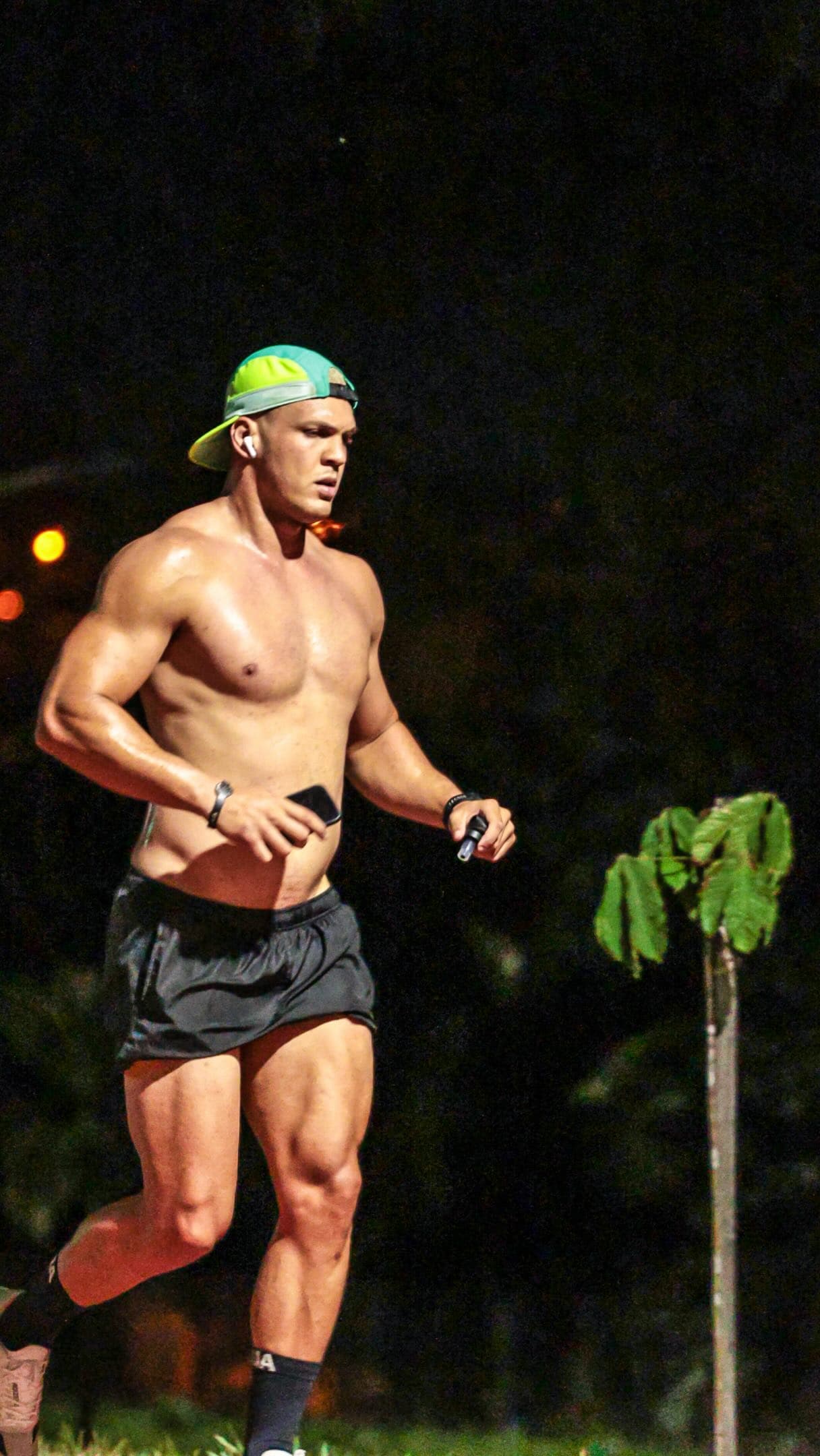 Matheus correndo à noite, sem camisa, de boné verde